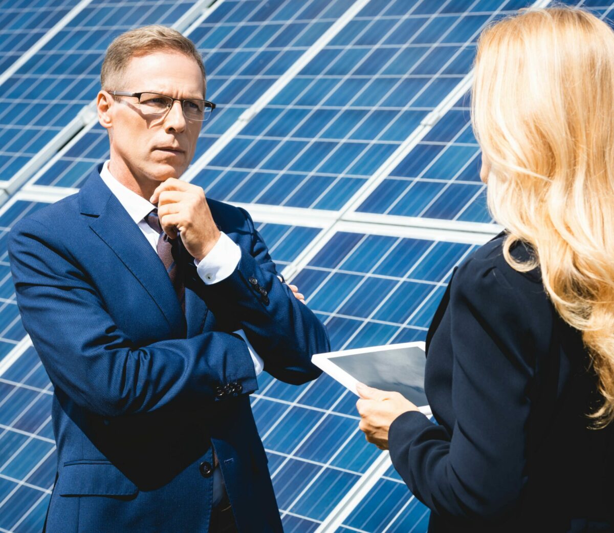 Handsome businessman and businesswoman talking and holding digital tablet with solar panels on the side